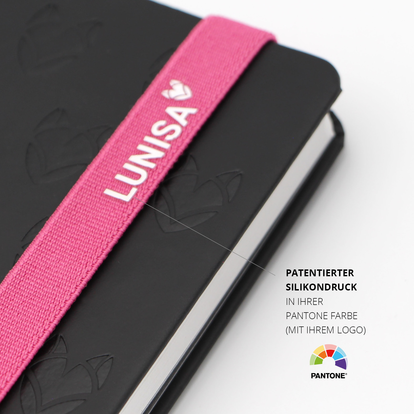Nahaufnahme des pinken Lanybands mit weißem Silikondruck des Lunisa-Logos. Der patentierte Aufdruck ist in Pantone-Farbe personalisierbar und harmoniert mit dem geprägten schwarzen Einband im Allover-Design.